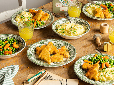 Dino Nuggets Mehrere Teller mit Tofu Nuggets, Kartoffelpüree und Erbsen und Möhren mit Tischdekoration.