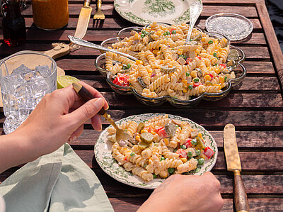 Nudelsalat Spirellis mit buntem Gemüse und heller Sauce auf Tellern mit Dekoration.