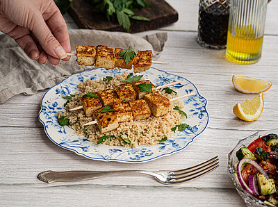 Harissa Tofu Spiesse mit Couscous Tofu-Spiesse auf Couscous auf einem Teller mit buntem Gemüse und Tischdekoration.