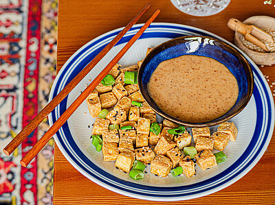 Tofu Puff Helle Tofustückchen mit Lauch auf einem Teller mit Dip und Tischdekoration.