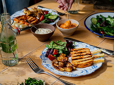 Vegane Rippchen Gegrillte Tofu-Rippchen und Kartofellspalten mit Salat auf 2 Tellern mit Tischdekoration.
