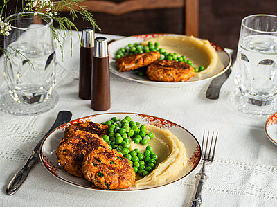 Tofu Frikadellen Tofu-Frikadellen mit Kartoffelpüree und Erbsen auf 2 Tellern mit Tischdekoration.