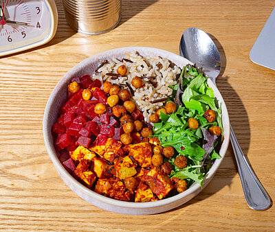 Rote Bete Kichererbsen-Curry Tofuwürfel mit rote Bete Würfel, Kichererbsen und Salat an Reis in einer Schüssel mit Tischdekoration.