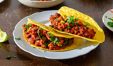 Tacos 3 Tacos mit rotem Sojagehacktem auf Tellern mit Tischdekoration.