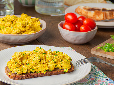 Eine Brotscheibe mit zerbröseltem, gewürztem Tofu und Kräutern.