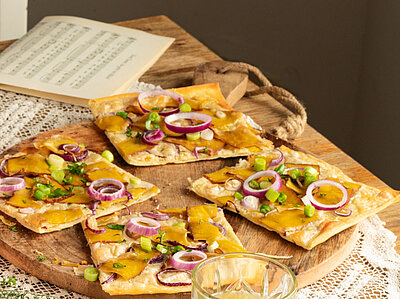 Vlammkuchen Vlammkuchen auf 2 Tellern und einem Holzbrett mit Zweibeln, Tofu und Lauch mit Tischdekoration.