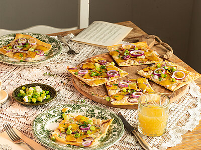 Vlammkuchen Vlammkuchen auf 2 Tellern und einem Holzbrett mit Zweibeln, Tofu und Lauch mit Tischdekoration.